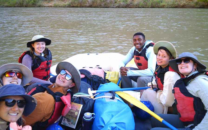 Seven people wearing life jackets sit in a raft and smile at the camera. 
